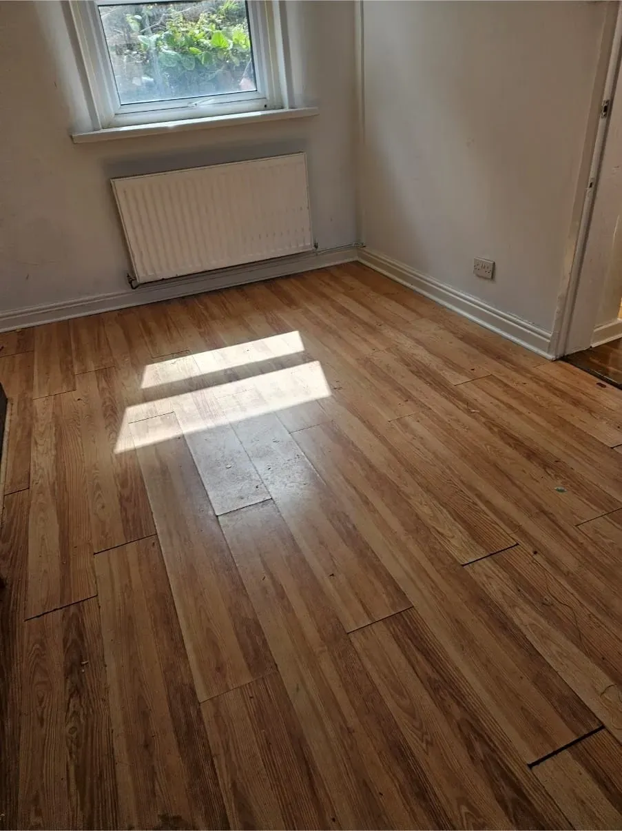 Empty room with wooden laminate flooring and a window after a professional house clearance service.